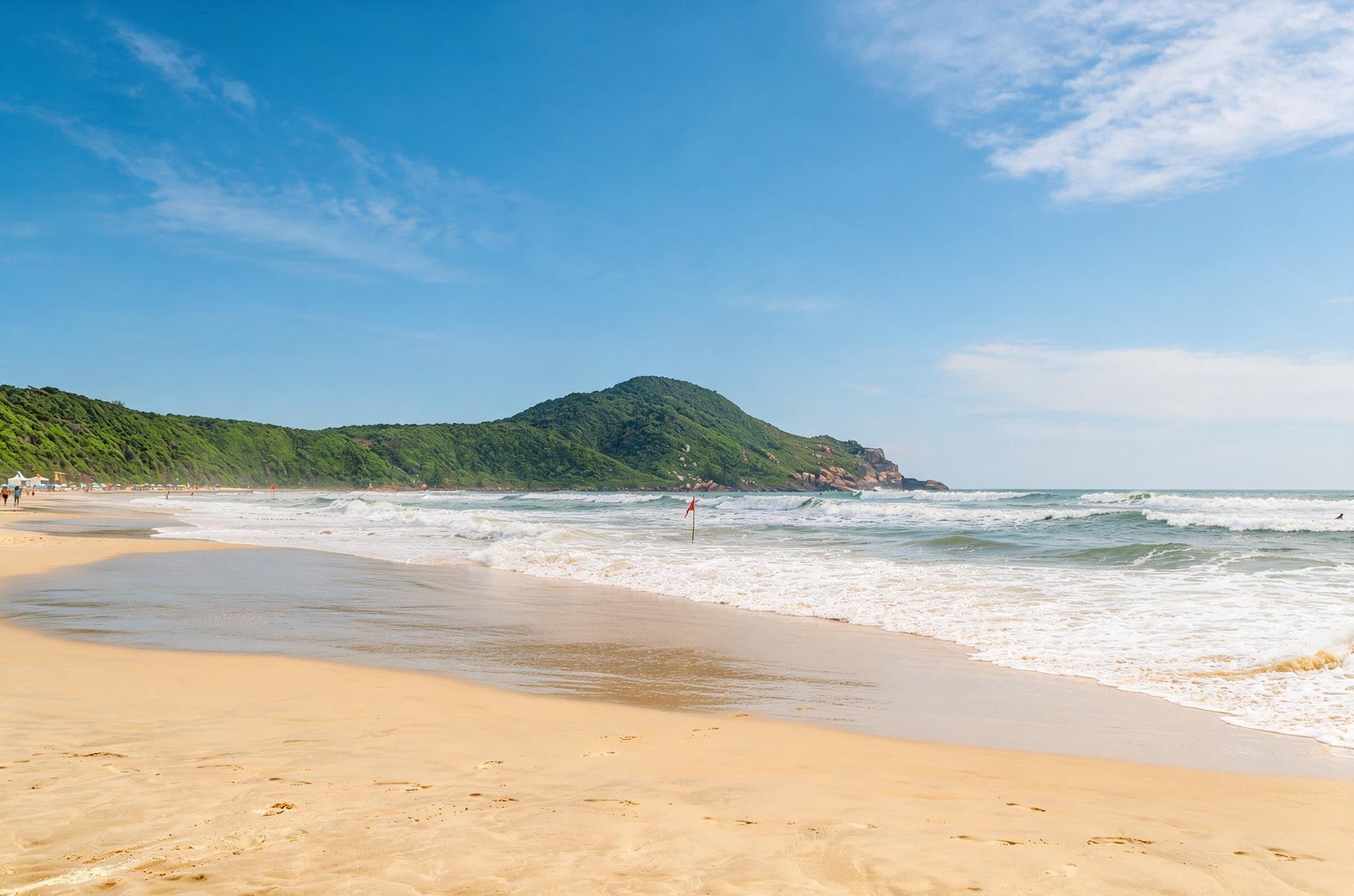 A beach with a sandy shore, waves, and a green hill in the background.
