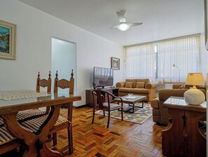 Ein Wohnzimmer mit Holzesstisch, Stühlen, einer Couch und einem Fernseher.