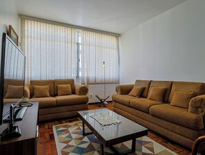 Ein Wohnzimmer mit zwei braunen Sofas, einem Glastisch und einem Fernseher auf einem Holzständer.