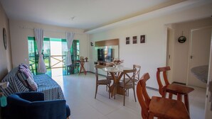 A living room with a sofa, a dining table with chairs, a TV, and a window with curtains.