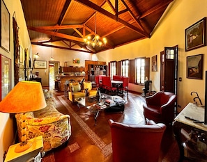A spacious living room with wooden beams, a chandelier, and a variety of seating including a sofa, chairs, and a coffee table. - Chácara com piscina, WiFi e lazer completo - SP (Bragança Paulista)