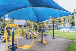 An outdoor gym with exercise equipment under a blue canopy.