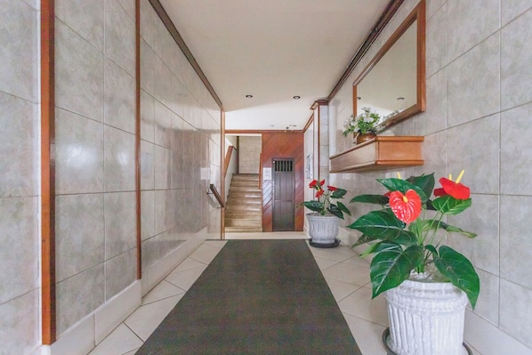 A hallway with tiled walls, a carpeted floor, a wooden staircase, and potted plants.