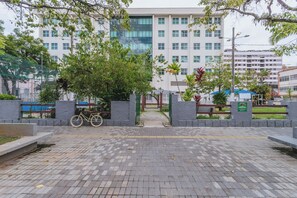 A paved walkway leading to a building with a modern design, surrounded by greenery and a bicycle parked by the entrance.