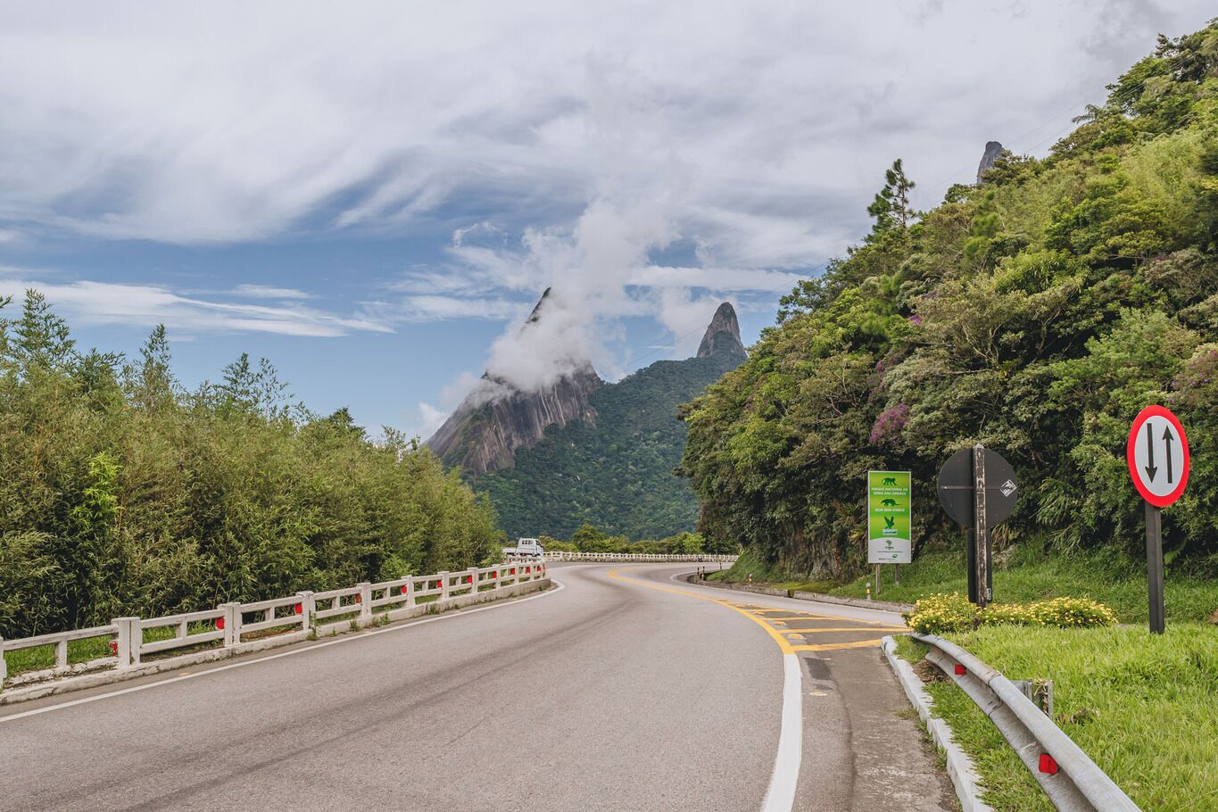 A road with a guardrail, a mountain in the background, and a sign indicating a two-way traffic area.