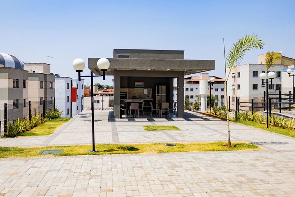 A modern outdoor seating area with tables and chairs, surrounded by a paved walkway and greenery.