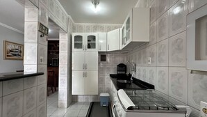 A kitchen with white cabinets, a black countertop, and a built-in stove. - Apto aconchegante c Wi-Fi e varanda para descansar (Caraguatatuba)