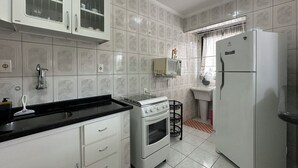 A kitchen with white cabinets, a black countertop, a stove, a microwave, and a refrigerator. - Apto aconchegante c Wi-Fi e varanda para descansar (Caraguatatuba)