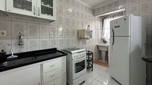 A kitchen with white cabinets, a black countertop, a stove, a microwave, and a refrigerator. - Apto aconchegante c Wi-Fi e varanda para descansar (Caraguatatuba)