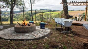 Uma área externa com espaço para sentar, uma fogueira, uma banheira branca e um pérgola.