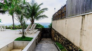 Un sendero que lleva a una zona de playa con sillas de descanso y una palmera.