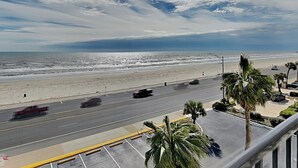 Vista a la playa desde un balcón, con una carretera al frente y palmeras.