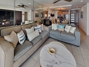 A modern living room with a sectional sofa, a marble coffee table, and a dining area with a chandelier. - By the Sea 507 | Upscale Condo w/ Gulf Front Balcony & Resort Pool (Galveston)