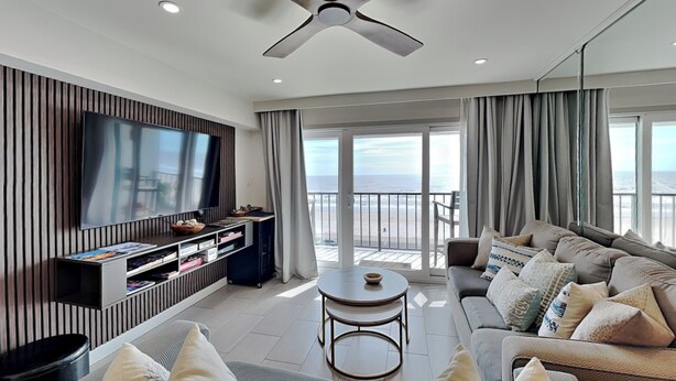Una sala de estar moderna con televisor de pantalla plana, un conjunto de sofás, una mesa de centro y un balcón con vista al mar.