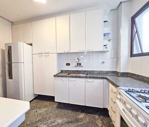 Eine kompakte Küche mit weißen Schränken, einer Arbeitsplatte aus Granit, einem Edelstahlkühlschrank und einem Gasherd.