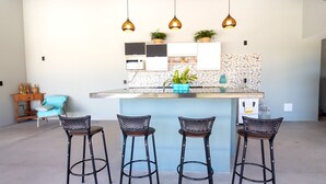 Una cucina moderna con isola centrale, sgabelli da bar, illuminazione a sospensione e una decorativa parete di fondo.