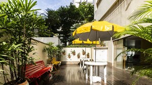 Een terras buiten met een houten terras, potplanten, een rode bank en een gele parasol voor schaduw.