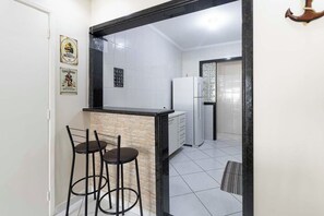 Eine kleine Küche mit schwarzem Arbeitsplatten, zwei Barhocker, einem Kühlschrank und einer gefliesten Spritzschutzwand.