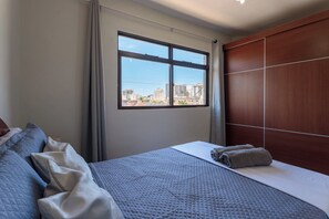 Ein Hotelzimmer mit großem Fenster, einem Bett mit gesteppter Bettdecke und einem Holzschrank.
