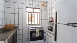Una cocina compacta con paredes de azulejos blancos, estufa a gas, horno empotrado, refrigerador y una ventana que proporciona luz natural.