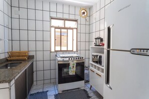 Eine kleine Küche mit weiß gefliesten Wänden, einem Gasherd, einem Backofen, einem Kühlschrank und einem Fenster für natürliches Licht.