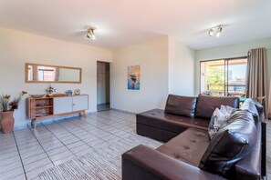 Ein modernes Wohnzimmer mit einer Sofagarnitur, einem Holzkabinett und einem großen Fenster mit Vorhängen.