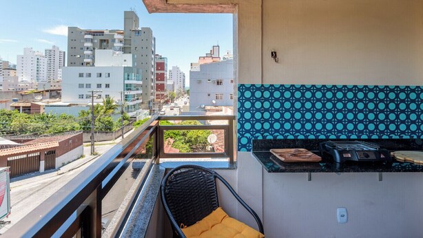 Un balcón con vistas a un paisaje urbano, una pequeña zona de cocina al aire libre y una silla de mimbre.