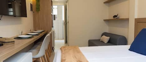 A hotel room with a bed, a desk with a chair, a small sofa, and a TV mounted on the wall.