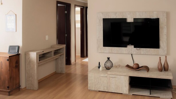 Een woonkamer met een aan de muur bevestigde televisie, houten kasten en een kleine tafel met decoratieve objecten.