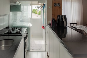 A compact kitchen with a gas stove, a coffee maker, and a dining area with a table and chairs. - Apto com churrasqueira, Wi-Fi e ótima localização (Curitiba)