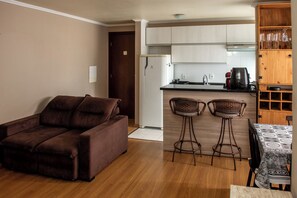 A living room with a brown sofa and two wicker bar stools. - Apto com churrasqueira, Wi-Fi e ótima localização (Curitiba)