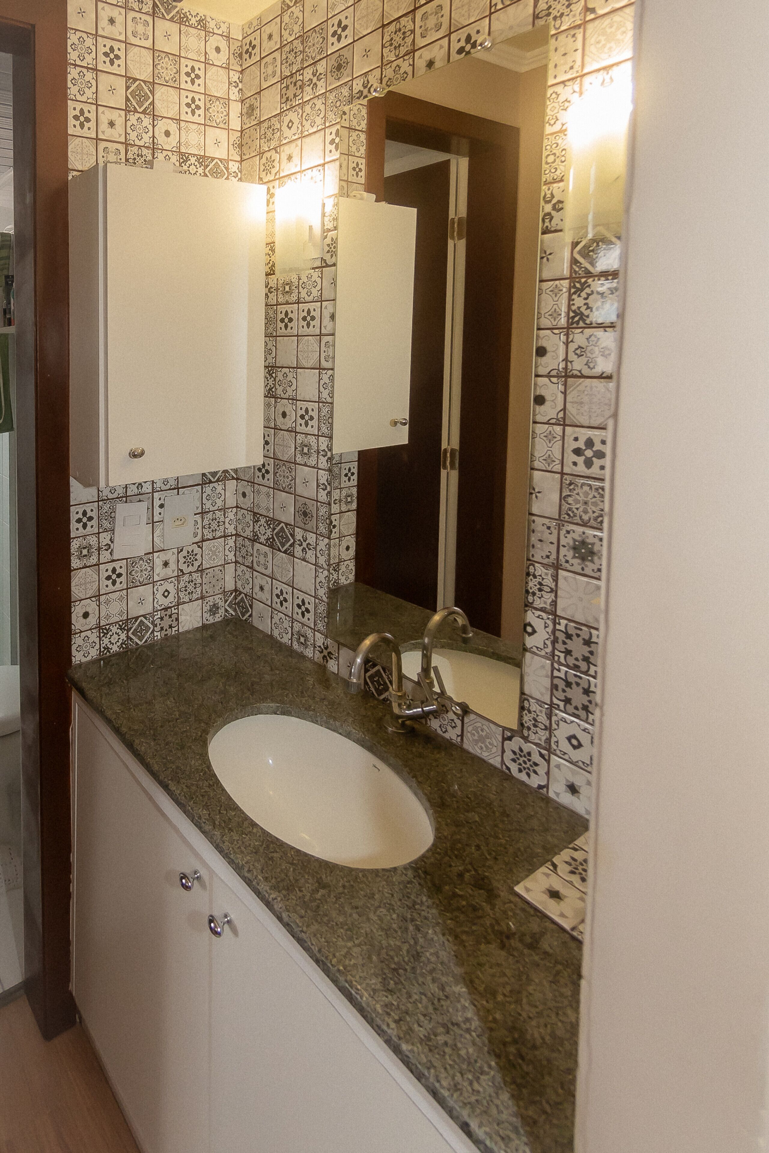 Een badkamer met een wastafel, spiegel en betegelde vloer.