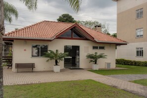 A two-story building with a red-tiled roof, a front entrance, and potted plants. - Apto com churrasqueira, Wi-Fi e ótima localização (Curitiba)