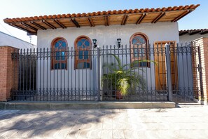Uma casa com portão de metal, três janelas em arco e telhado telhado.