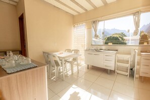 A bright kitchen with a dining area, white cabinets, and a window with a mountain view. - Apto c/ Wi-fi,  garagem e vista das montanhas (Angra dos Reis)