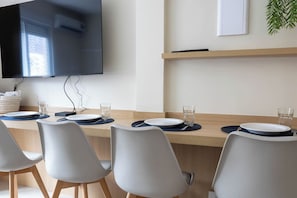 Uma sala de conferências com uma mesa comprida, cadeiras brancas e uma TV de tela plana fixada na parede.
