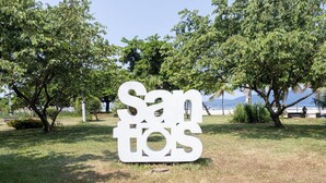 A large white sign with the text "Sanitos" in a park with trees and a beach in the background. - Apartamento Moderno com Wi-Fi em frente a praia (Santos)