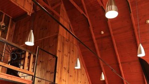 A spacious room with a high ceiling, wooden beams, a staircase, and a dining area with a table and chairs.
