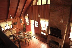 Un intérieur chaleureux et rustique, avec des poutres en bois, une cheminée et un coin repas où une table est dressée pour quatre personnes.