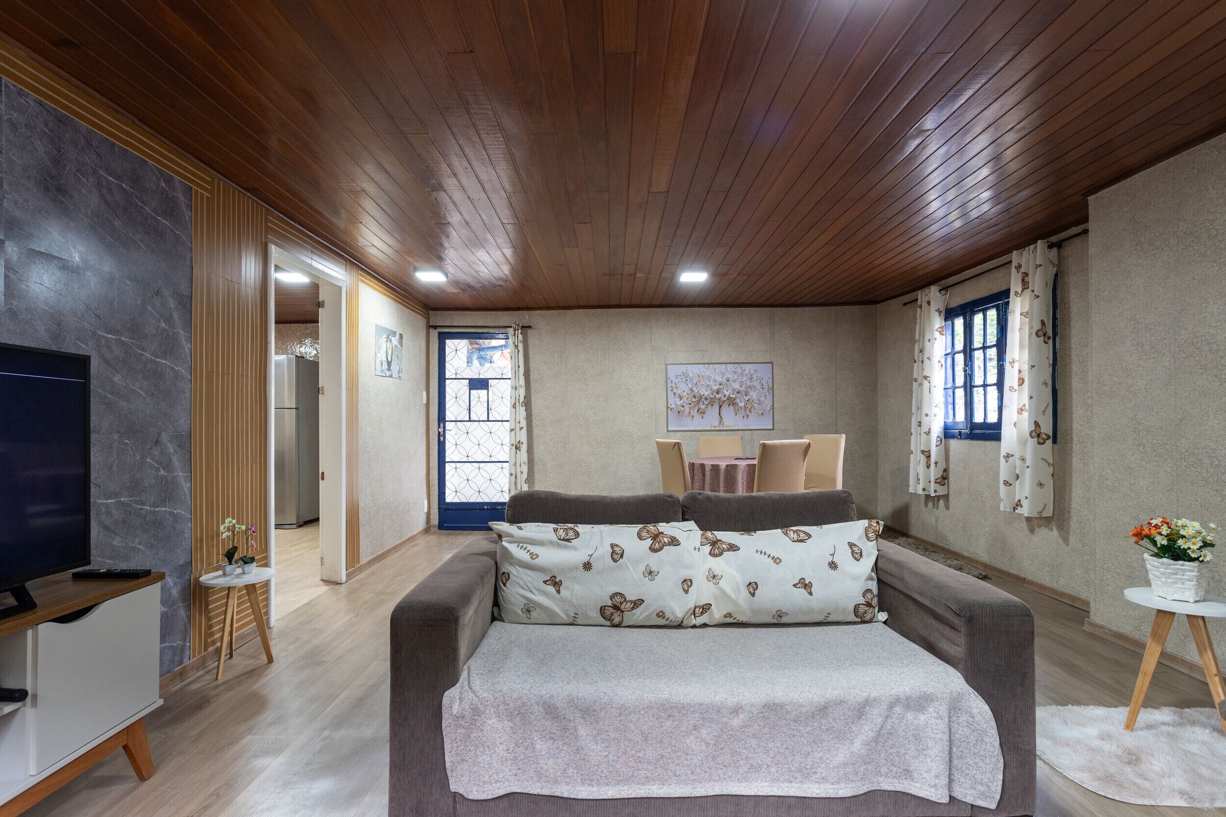 A modern bedroom with a wooden ceiling, a large bed with patterned pillows, a TV, and a small table with flowers.