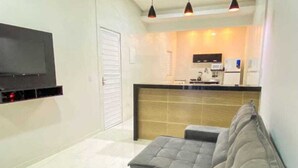 Un soggiorno moderno con un divano grigio, una televisione a schermo piatto montata a parete e un angolo cottura sullo sfondo.