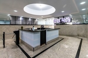 Eine moderne Hotelhalle mit einer zentralen Rezeption, einer großen digitalen Anzeige und einer Wanduhr.