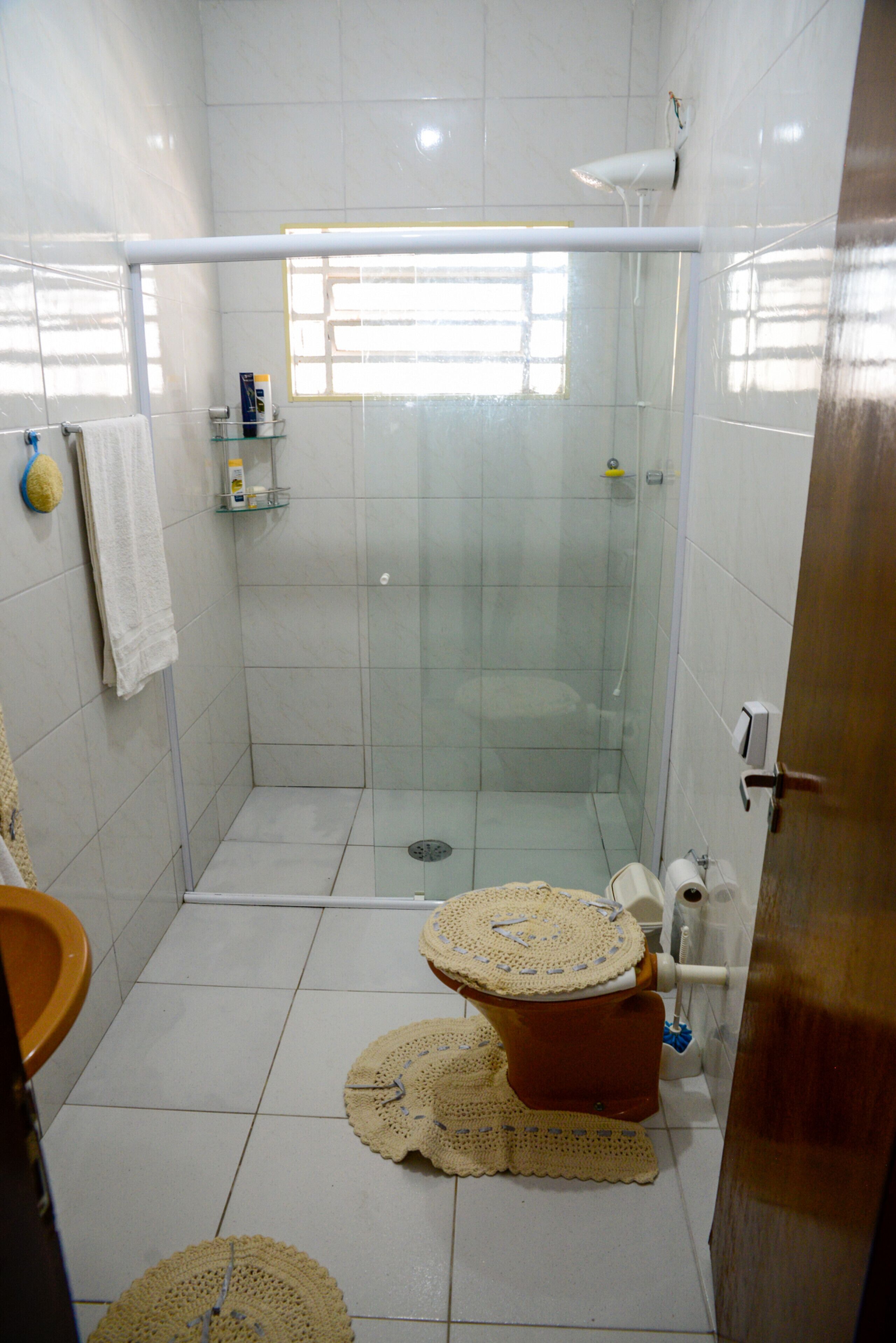 Un baño con cabina de ducha de vidrio, un inodoro con una alfombra decorativa y un perchero para toallas.