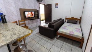 Ein kleines Zimmer mit Bett, Sofa, Fernseher, Esstisch und Stuhl.