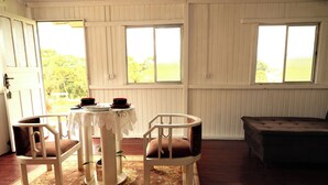 Habitació amb taula preparada per a dues persones, una banca i vista a vegetació a l'exterior.