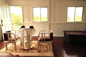 A room with a table set for two, a bench, and a view of greenery outside.