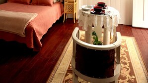 Un dormitori amb un llit, dues làmpades de nit, un penjoll, una finestra amb cortines, una taula petita amb una tovallola de punt de ganc i un quadre amb marc a la paret.