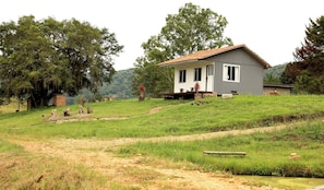 A single-story house with a sloped roof, a porch with a bench, and a small garden area with hay bales.