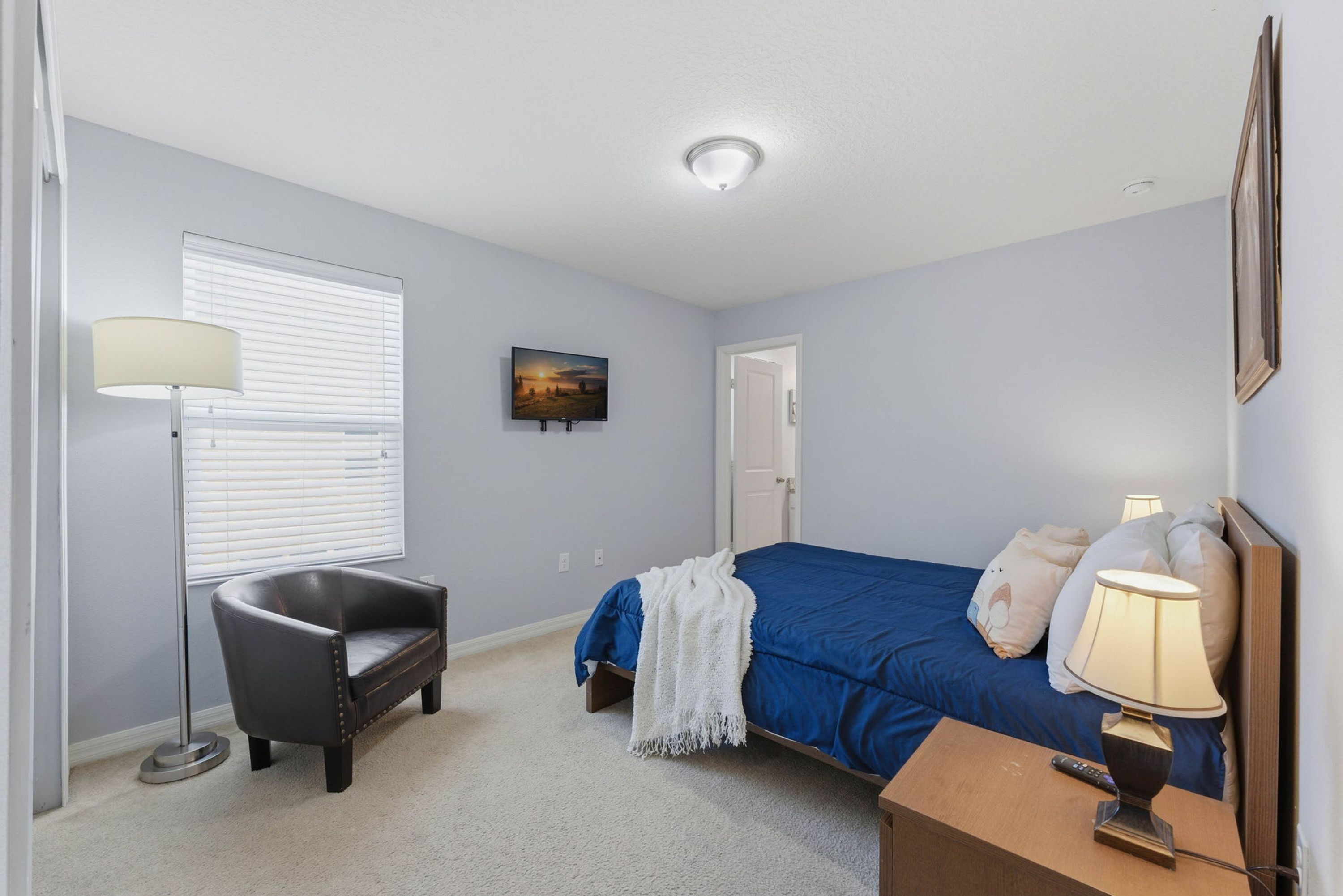 A bedroom with a bed, a chair, a lamp, a painting, and a door.