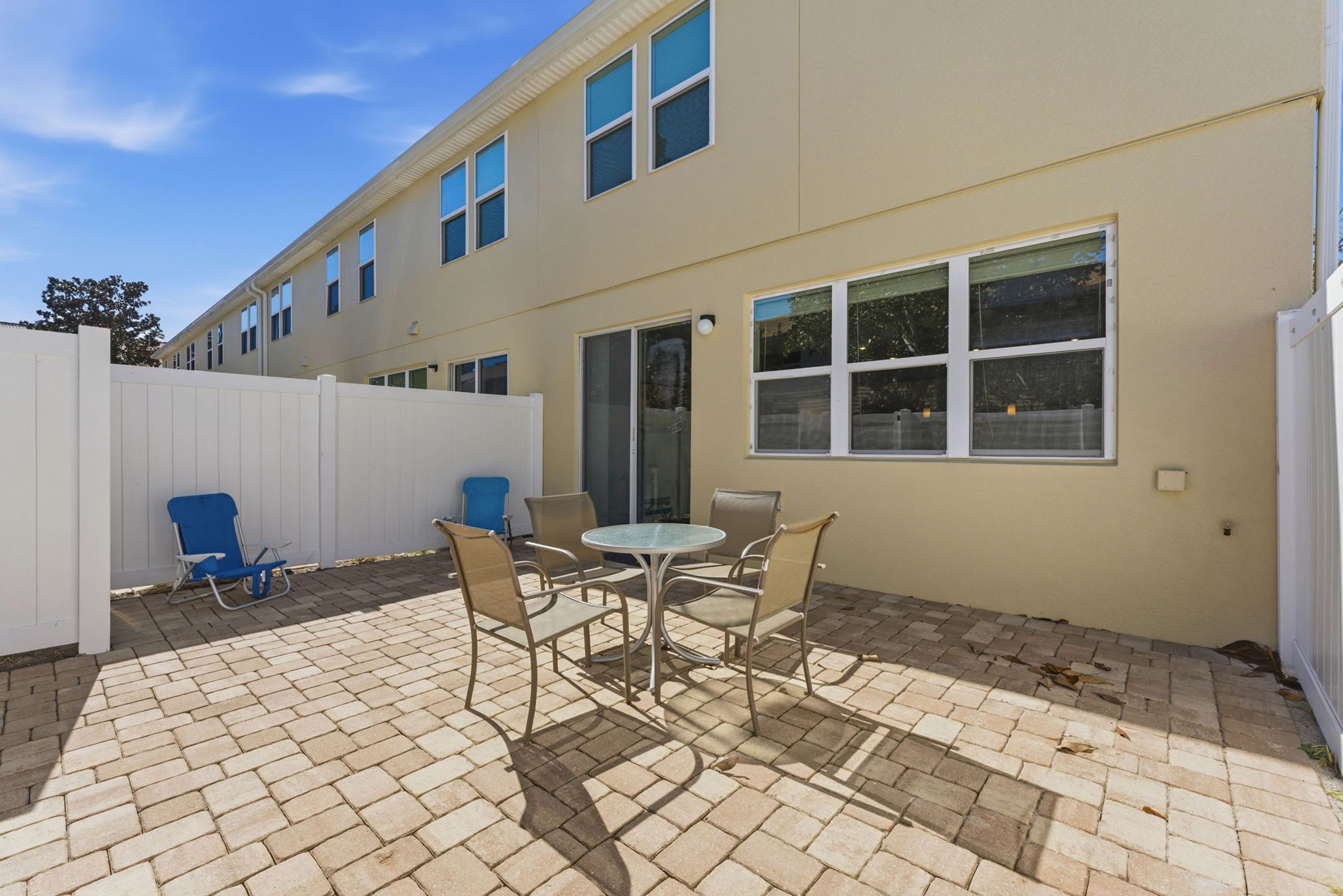 A patio with a table and chairs, a white fence, and a building with windows.
